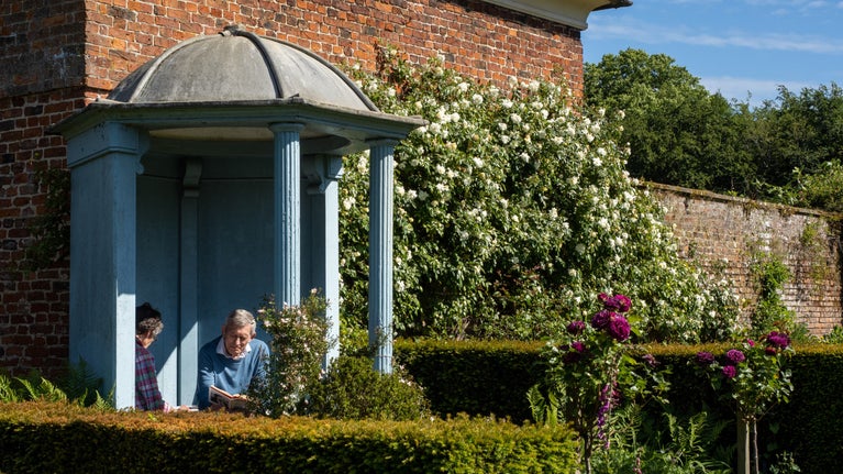 Visitors reading inside the Blue Temple, surrounded by the colourful flowers of Gunby Gardens, Lincolnshire.